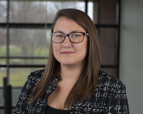 Megan Belfield, in glasses and a patterned blazer, stands in front of a window.